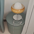 Seen from above on a green round nightstand, this Clérachic table lamp shows its white globe in the amber bowl and the cord below.