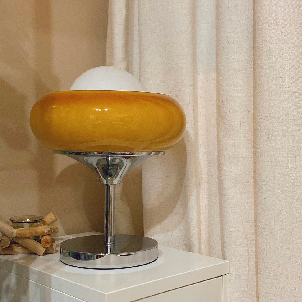 Close view of this Clérachic table lamp on a white cabinet against a linen curtain, its amber shade glossy and the globe pale.