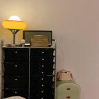 On top of a black drawer unit, this Clérachic table lamp glows next to a retro radio against a pale wall.