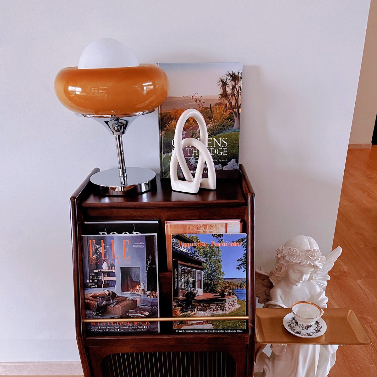On a dark wood cabinet with magazines, this Clérachic table lamp shows its deep amber shade next to a white ornament and a figurine.