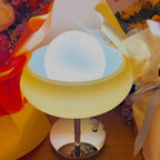 A very close, brightly lit view of this Clérachic table lamp among yellow wrapping paper and flowers, with its chrome base below.