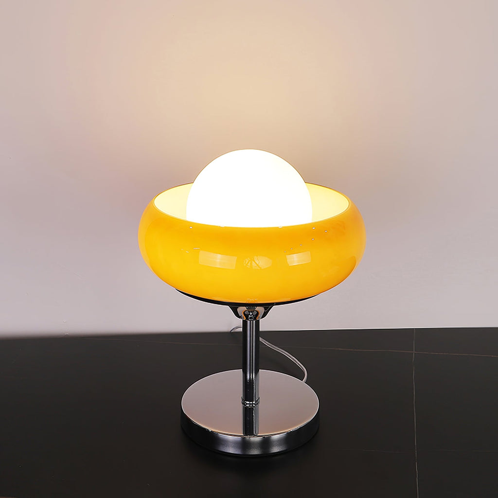 This Clérachic table lamp lit on a black surface, its white globe inside a bright yellow bowl shade, over a chrome base.