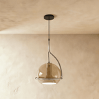 Clérachic champagne glass pendant light on a curved chrome arm, its amber globe shade hanging from a warm plaster ceiling.