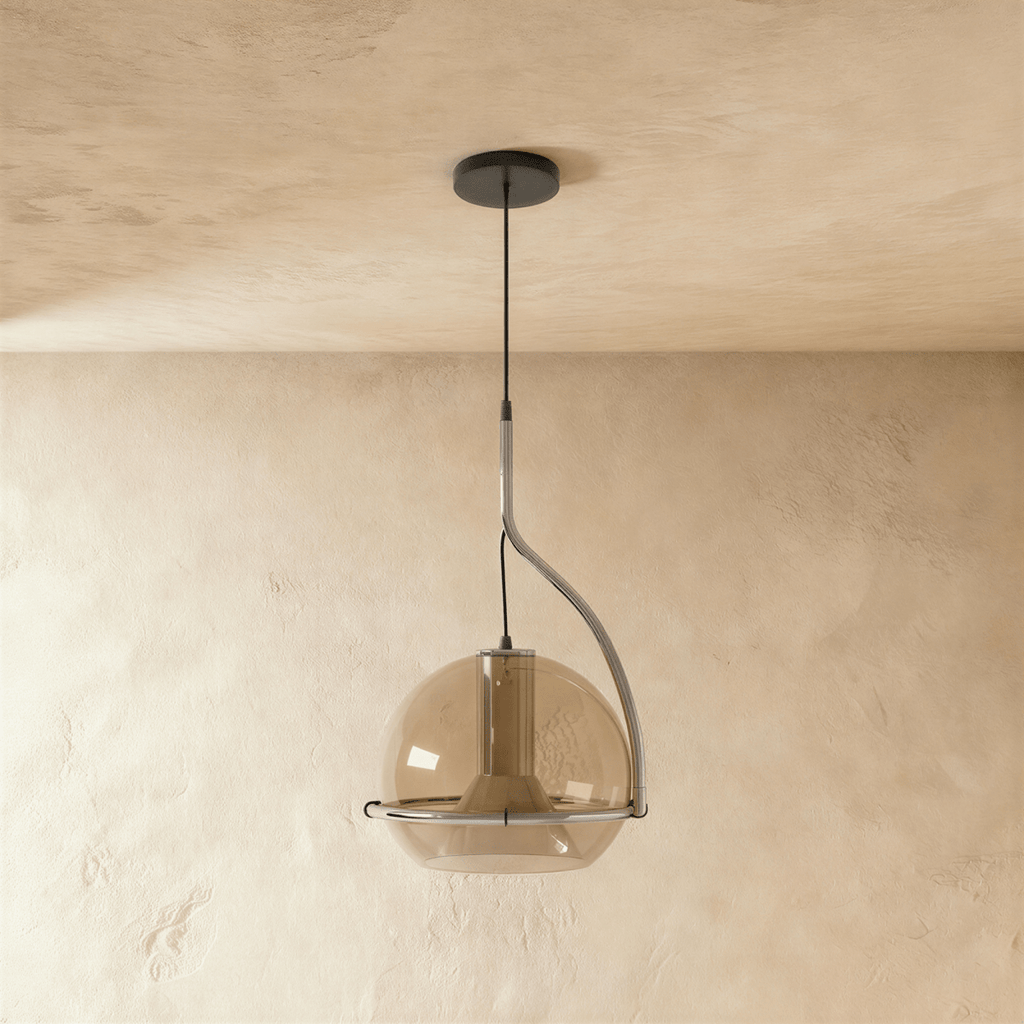Clérachic pendant light with a smoked amber glass globe and chrome stem, hanging low against a plain plaster wall.