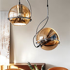 Two Clérachic champagne glass pendant lights with chrome frames hang above a walnut sideboard near a framed winter print.
