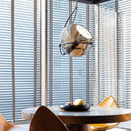 Clérachic amber glass pendant light hangs over a round dining table, its chrome arm catching light from slatted blinds.