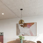 Clérachic champagne glass pendant light hangs beside an abstract painting, its globe shade glowing above a dining table.