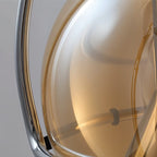 Macro detail of the Clérachic pendant's smoked amber glass and polished chrome trim, showing the curve of the globe shade.