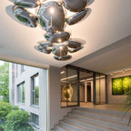 Two Clérachic 6-head Chrome Ceiling Lights lead a glass-walled foyer past a stone stair and hallway art.