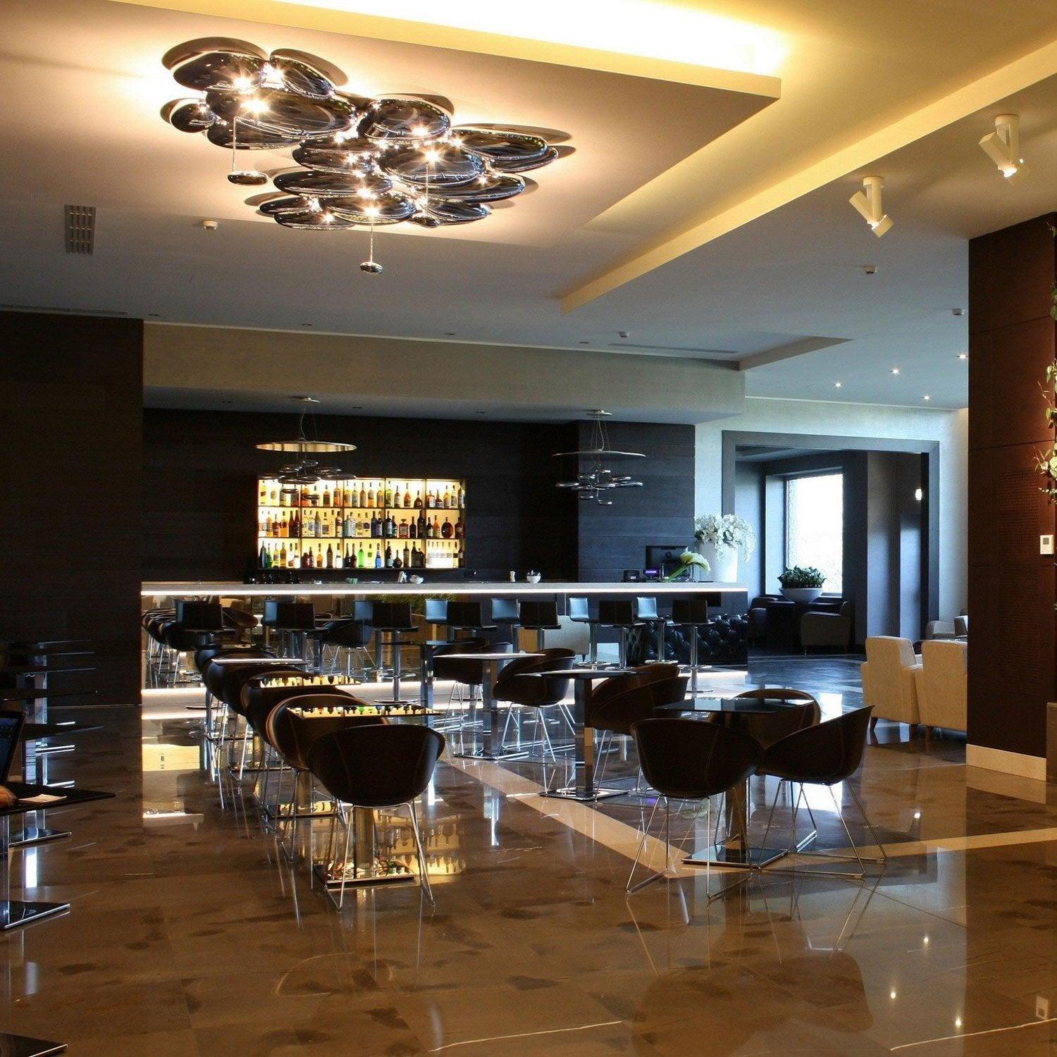 Clérachic Chrome Ceiling Light over a lounge with black chairs, polished marble floor, and a lit back bar.