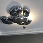 Clérachic 6-head Chrome Ceiling Light on a white ceiling, chrome pebbles haloed above a dark slatted wall.