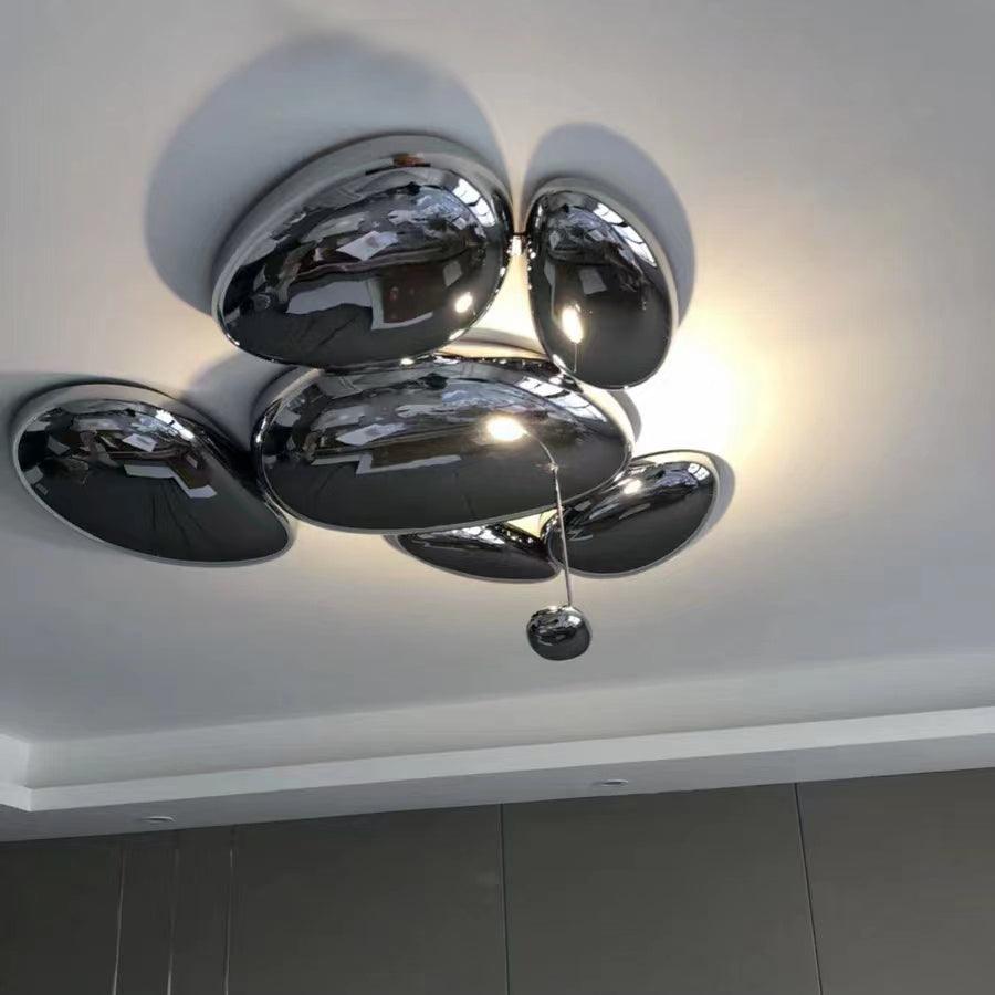Clérachic 6-head Chrome Ceiling Light on a white ceiling, chrome pebbles haloed above a dark slatted wall.
