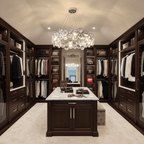 Clérachic crystal chandelier above the central island of a walk-in dressing room lined with dark wood wardrobes.
