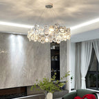 Round Clérachic crystal chandelier under a cove-lit ceiling, beside a grey stone feature wall and sheer curtains.