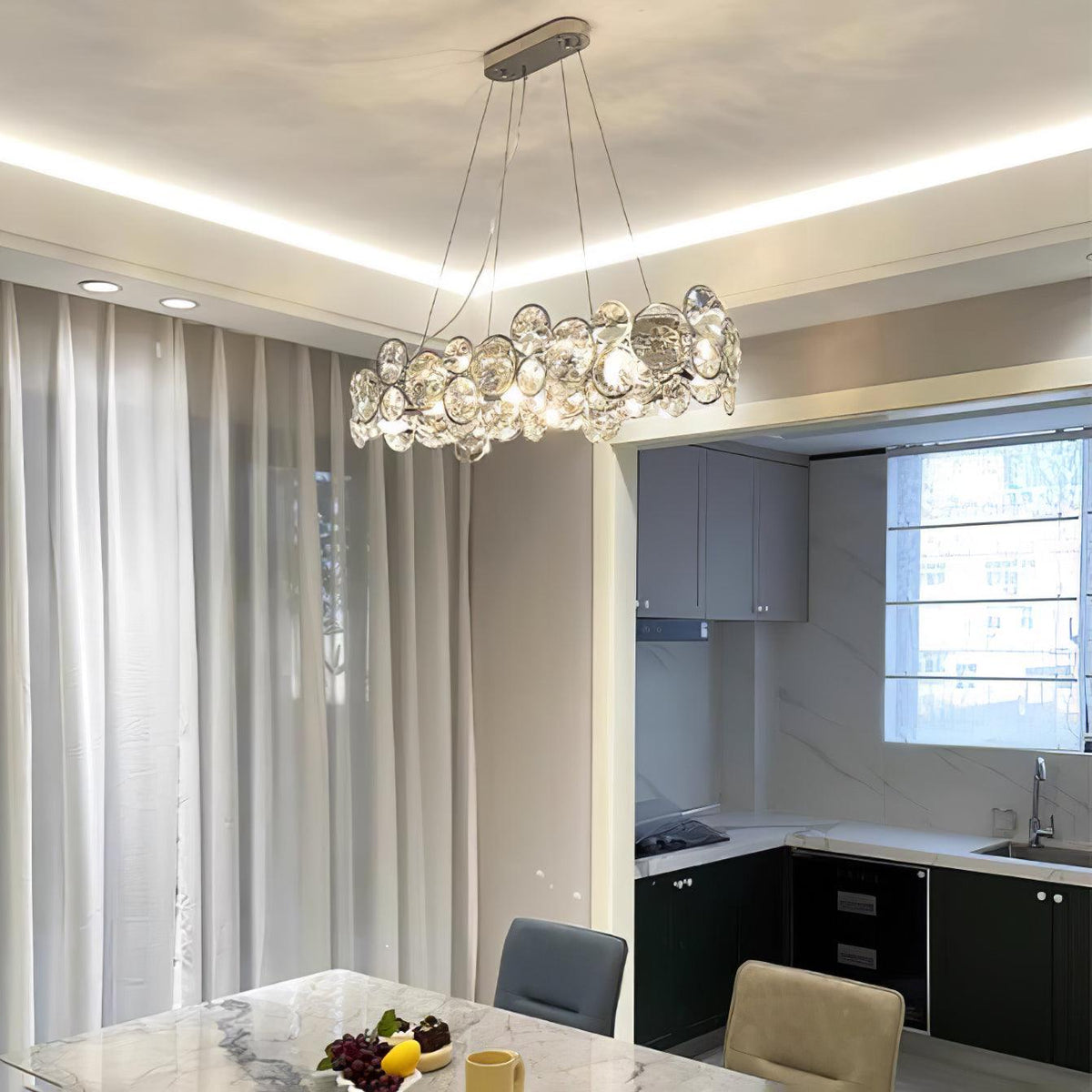Oval Clérachic chandelier under a ceiling with an LED cove, in a dining area that opens onto a dark kitchen.