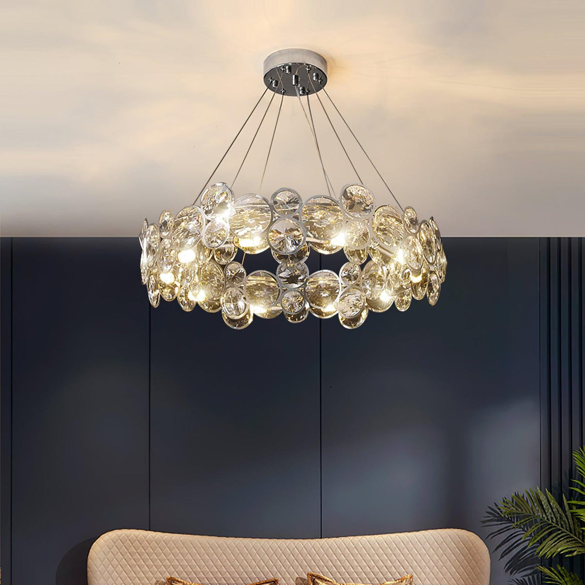 Low view of this Clérachic crystal chandelier lit against a navy wall, with a cream sofa back below.