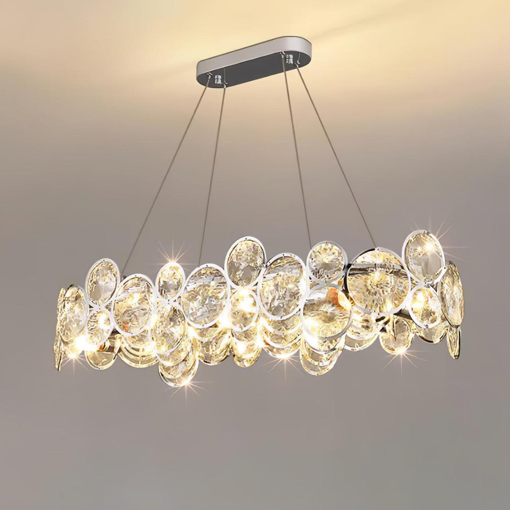 Oval Clérachic crystal chandelier lit and sparkling, hanging from a long chrome canopy against a grey wall.