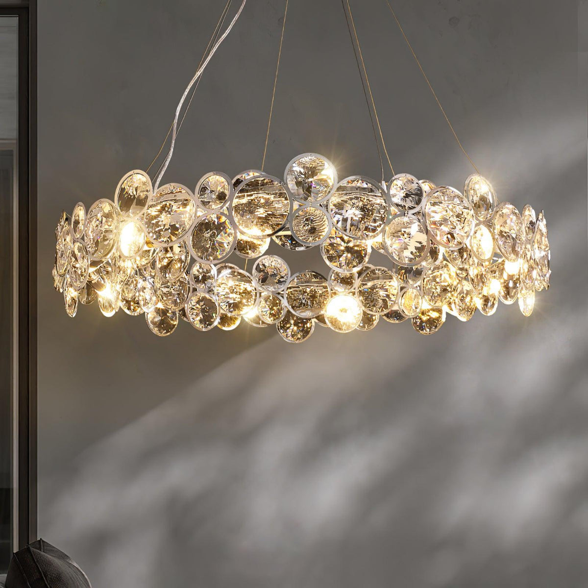 Side view of a Clérachic crystal chandelier lit, with its sparkling discs casting shadows on a grey wall.