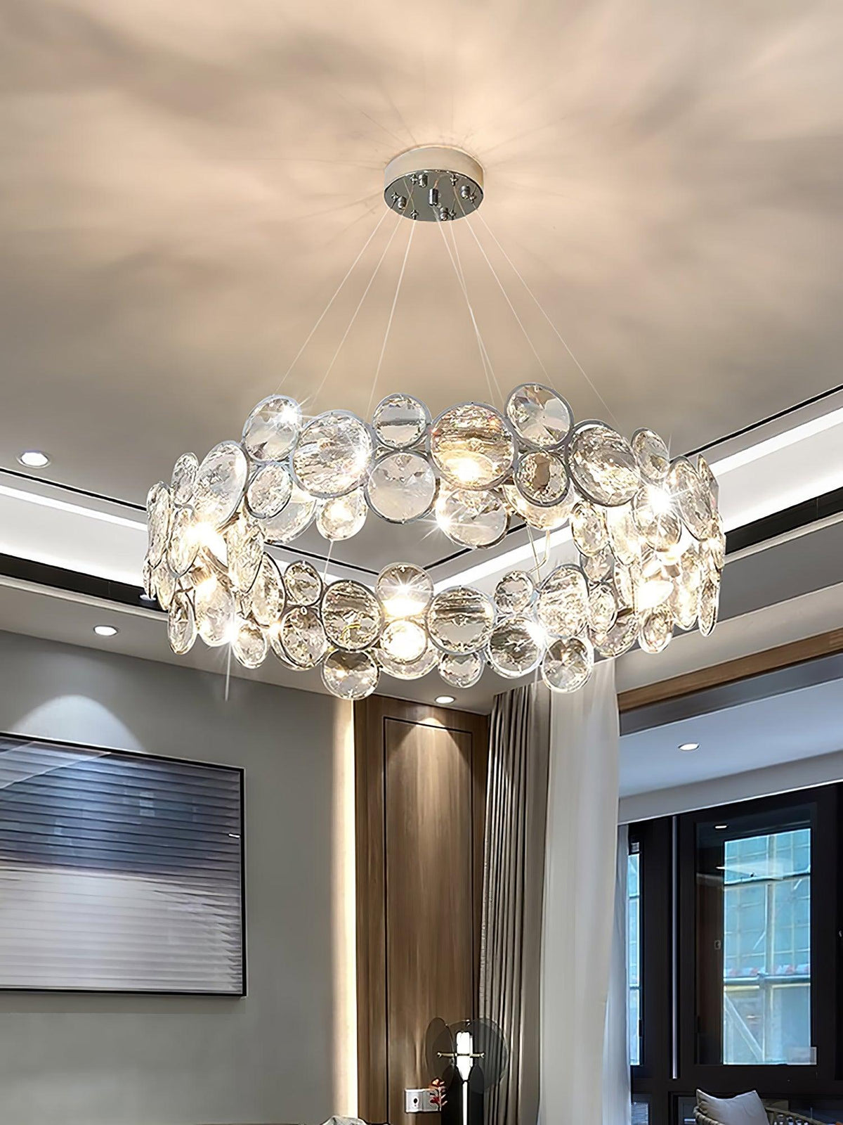 Round Clérachic chandelier in a living room with a wood-clad wall, a dark window and a cove-lit ceiling.