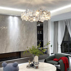 Round Clérachic crystal chandelier above a marble coffee table and a green armchair with a red throw.
