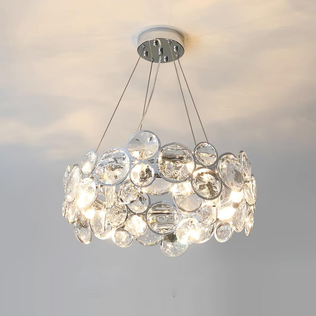 Round Clérachic crystal chandelier with a small chrome canopy, glowing warm against a pale ceiling and wall.