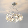 Round Clérachic crystal chandelier with a small chrome canopy, glowing warm against a pale ceiling and wall.