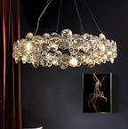 Wide view of a lit Clérachic crystal chandelier in a dark room, with a maroon curtain and a framed abstract print.