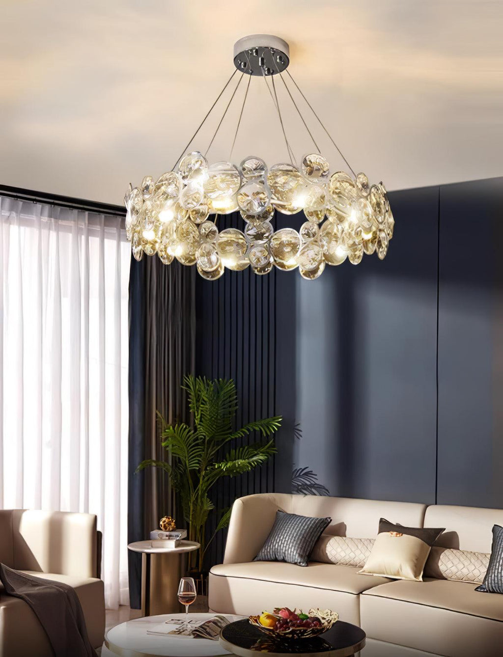 Clérachic crystal chandelier lit above a living room with a navy wall, a cream sofa and a potted palm.