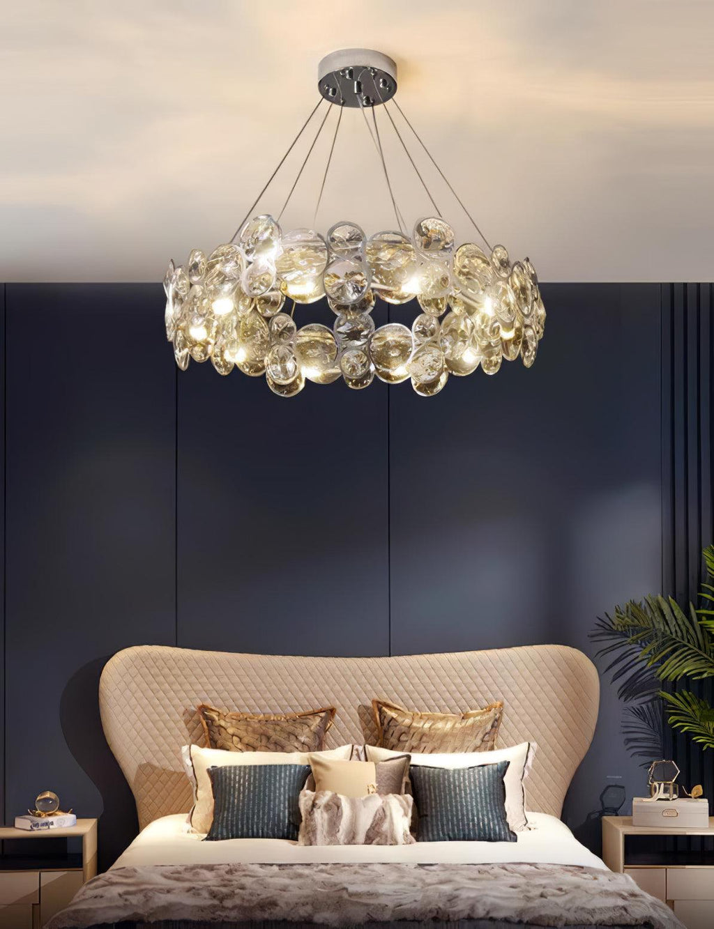 Clérachic crystal chandelier above a bed with a curved beige headboard and teal cushions, against a navy panelled wall.