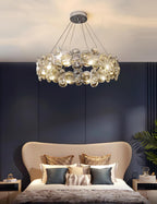 Clérachic crystal chandelier above a bed with a curved beige headboard and teal cushions, against a navy panelled wall.