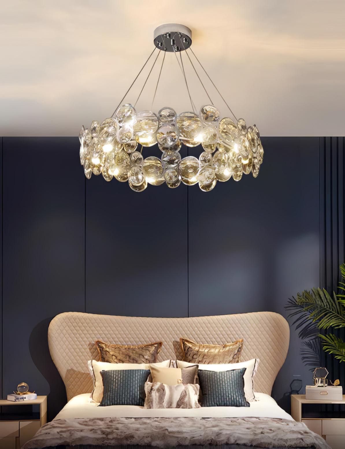 Clérachic crystal chandelier above a bed with a curved beige headboard and teal cushions, against a navy panelled wall.