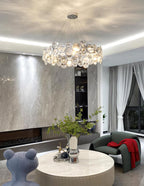 Round Clérachic chandelier seen above a coffee table with a vase of green stems, with the stone wall behind it.