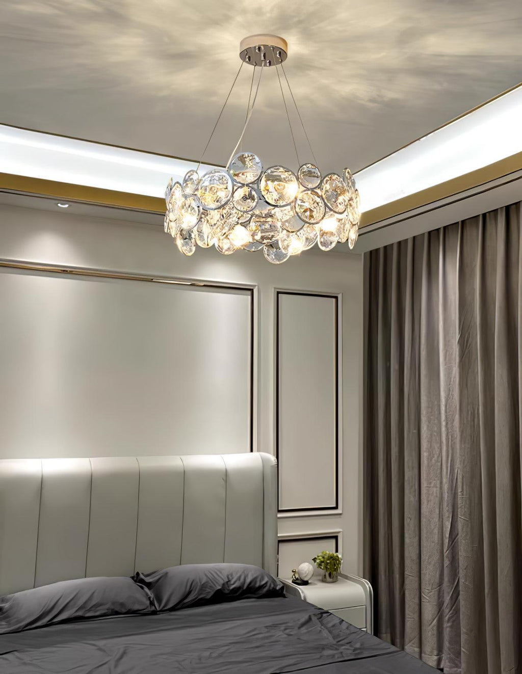 Clérachic crystal chandelier above a grey upholstered bed in a bedroom with panelled walls and grey curtains.