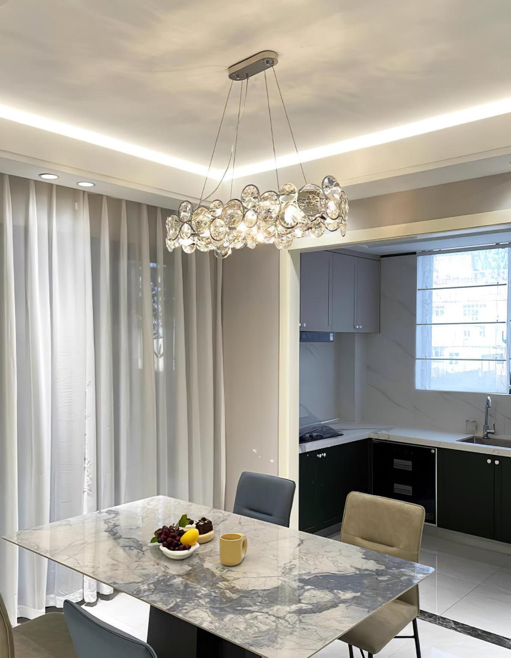 Oval Clérachic crystal chandelier over a marble dining table with a fruit bowl, with the kitchen beyond.