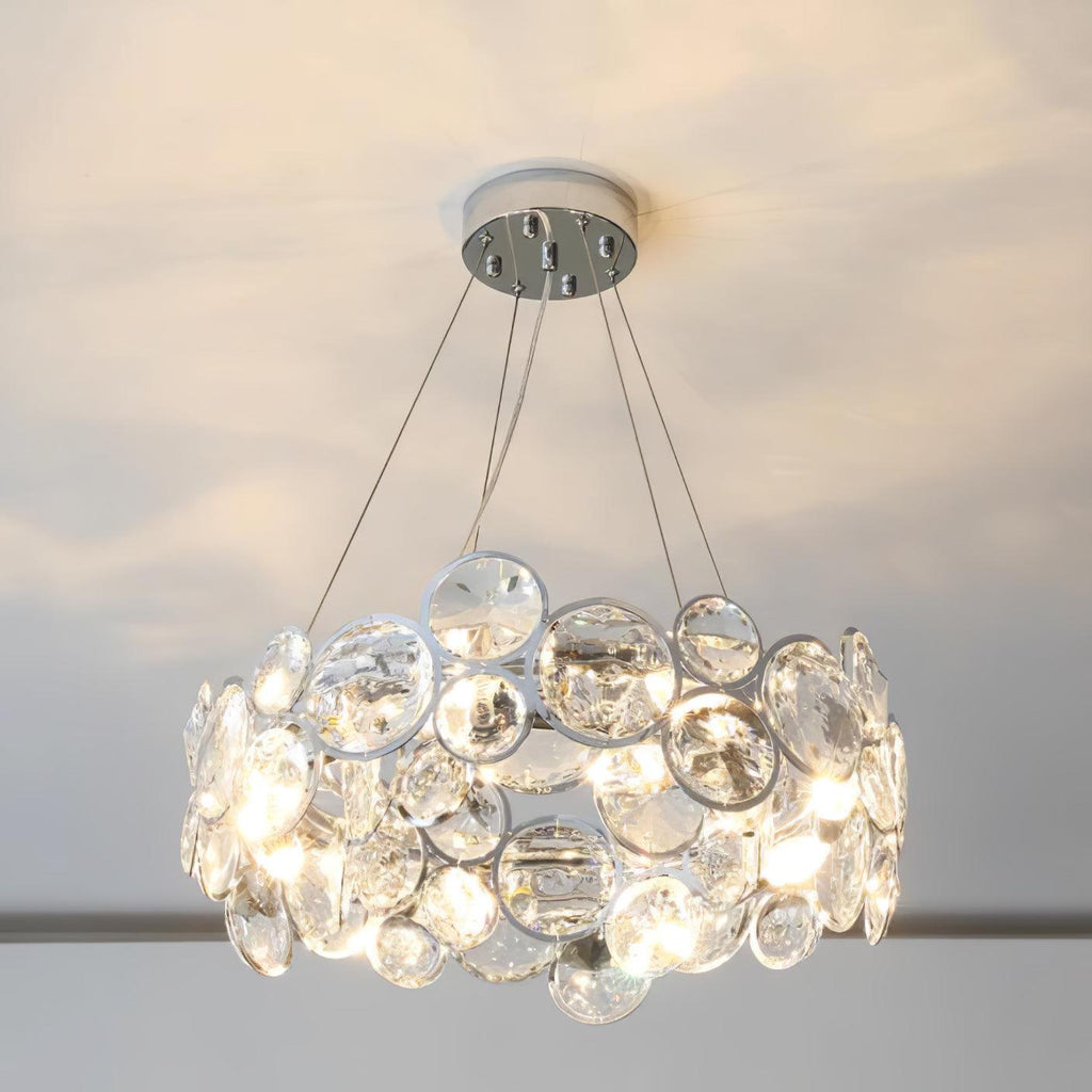 Round Clérachic crystal chandelier glowing under a pale ceiling, with the five cables meeting at a chrome canopy.
