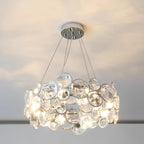 Round Clérachic crystal chandelier glowing under a pale ceiling, with the five cables meeting at a chrome canopy.