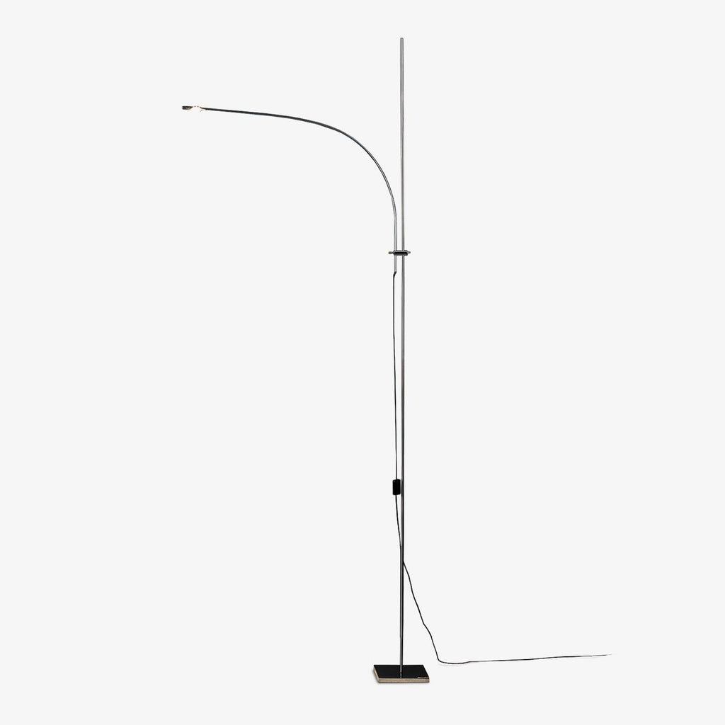 A Clérachic slender chrome floor lamp with a curved arm and square base, shown on a plain white backdrop with its cord trailing.