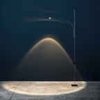 Against a deep blue wall, this Clérachic floor lamp throws an arched beam of warm light down onto a concrete floor.