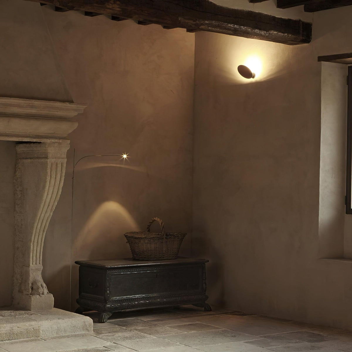 In a stone-walled room with a carved fireplace, this Clérachic floor lamp casts a soft arched pool of light on the plaster wall.
