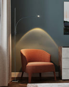 This Clérachic floor lamp rises beside a curtain, its warm arc of light falling over a rust-orange armchair.