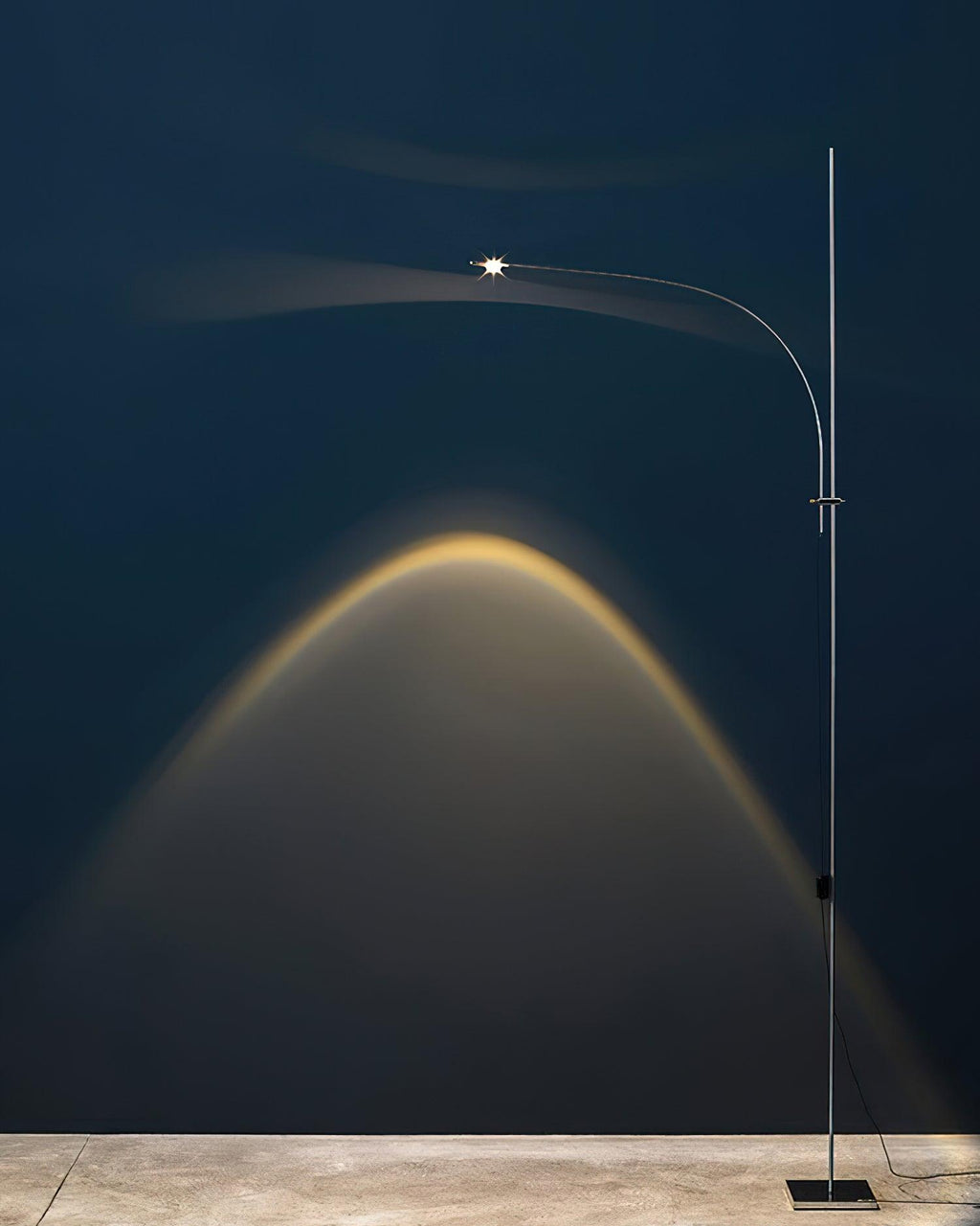 Tall and narrow, this Clérachic chrome floor lamp lights a deep navy wall with a warm arched beam above its square base.