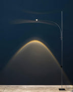 Tall and narrow, this Clérachic chrome floor lamp lights a deep navy wall with a warm arched beam above its square base.