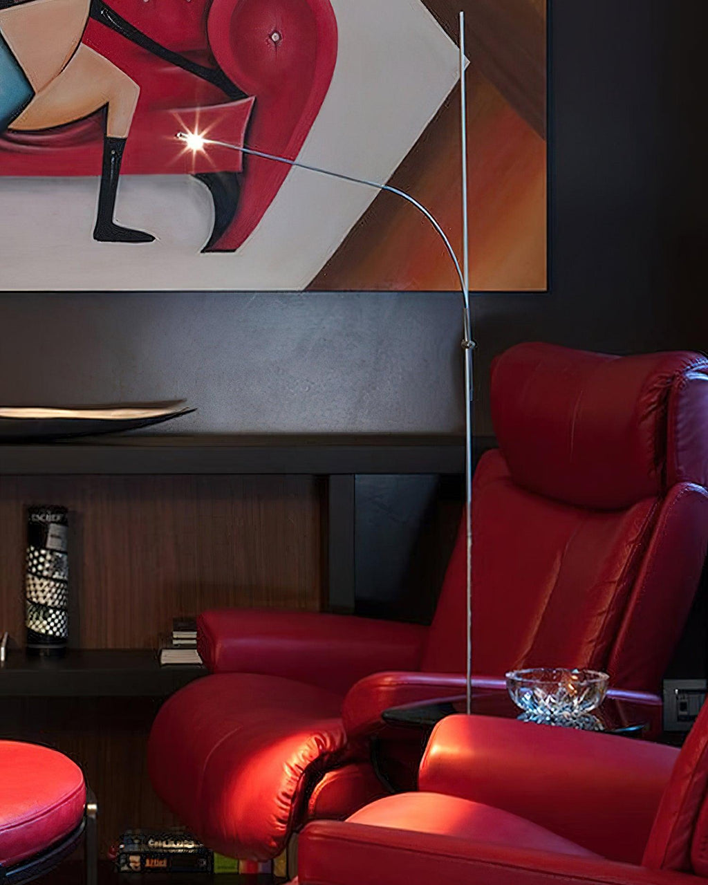 A Clérachic floor lamp curves above red leather armchairs beside a bold abstract painting, its light head glinting.