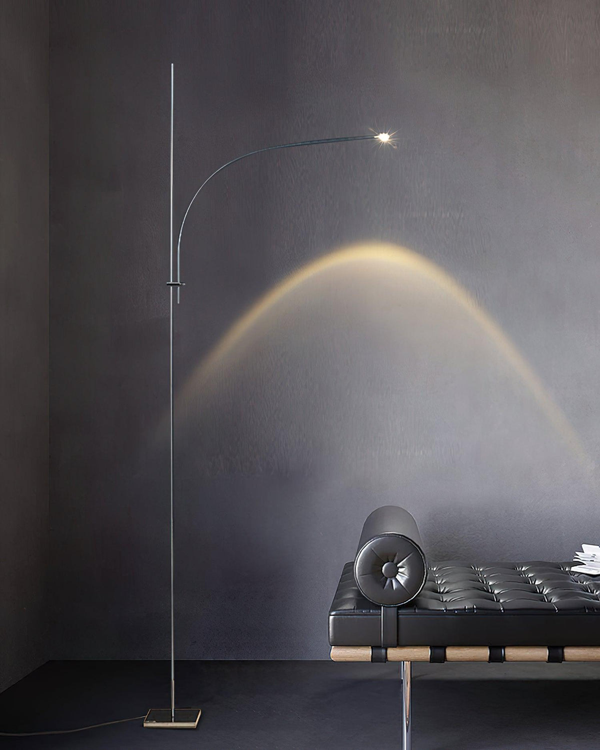 Beside a black leather bench, this Clérachic chrome floor lamp sends a soft arch of light across a dark grey wall.
