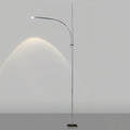 This Clérachic floor lamp on a light grey backdrop, its curved arm casting an arc of warm light on the wall.