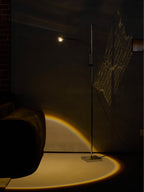 This Clérachic floor lamp lights a dim corner with a warm arc on the floor, beside a grey velvet sofa and a brick wall.