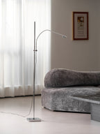 A wider view of this Clérachic chrome floor lamp by a grey velvet sofa, a framed poster on the wall behind.