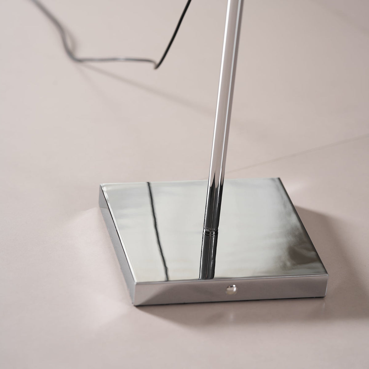 Close view of the square polished chrome base of this Clérachic floor lamp, with the pole and cord rising from it.