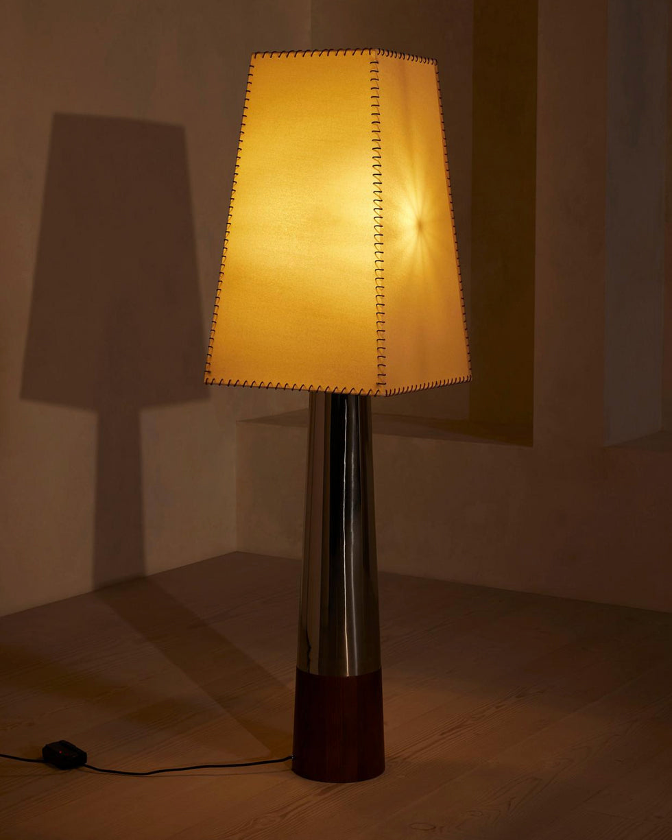 Warm amber light fills the tapered shade of this Clérachic floor lamp, with its cord and foot switch trailing across a wooden floor.