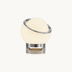 Glowing white glass globe with a tilted chrome ring on a short chrome base, shown on a plain white backdrop as this Clérachic table lamp.